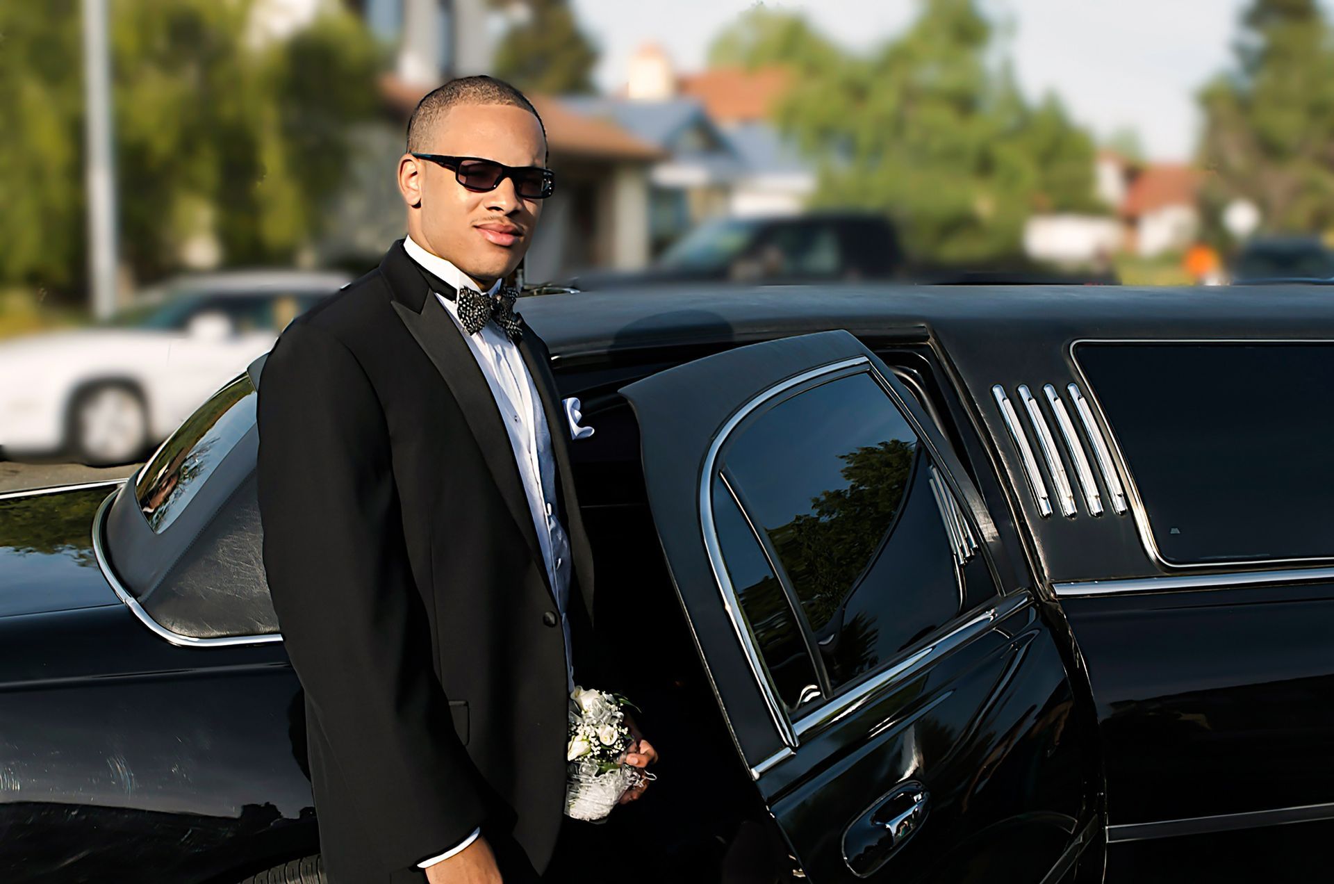 A man in a tuxedo is standing next to a black limousine.