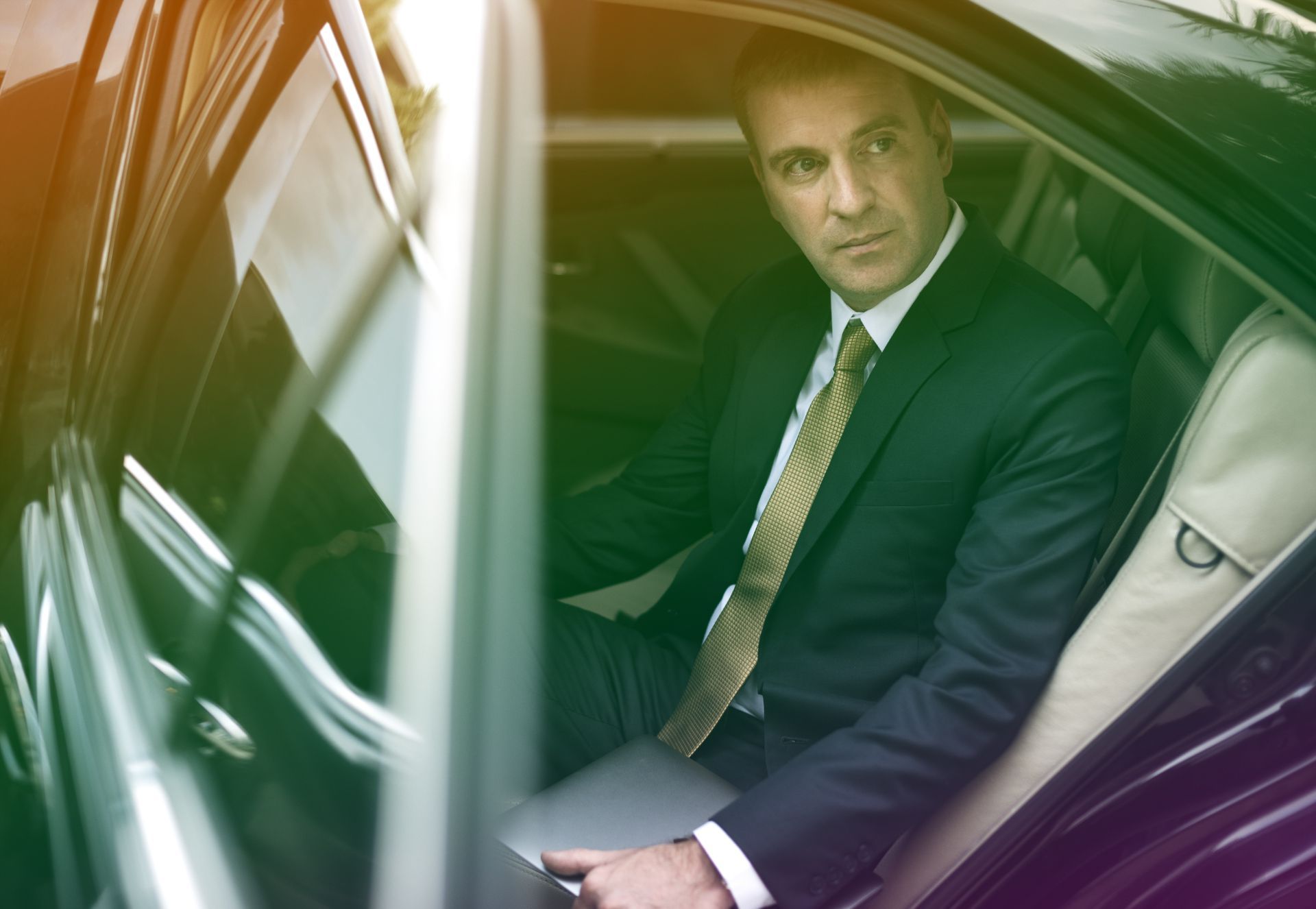 A man in a suit and tie is sitting in the back seat of a car.