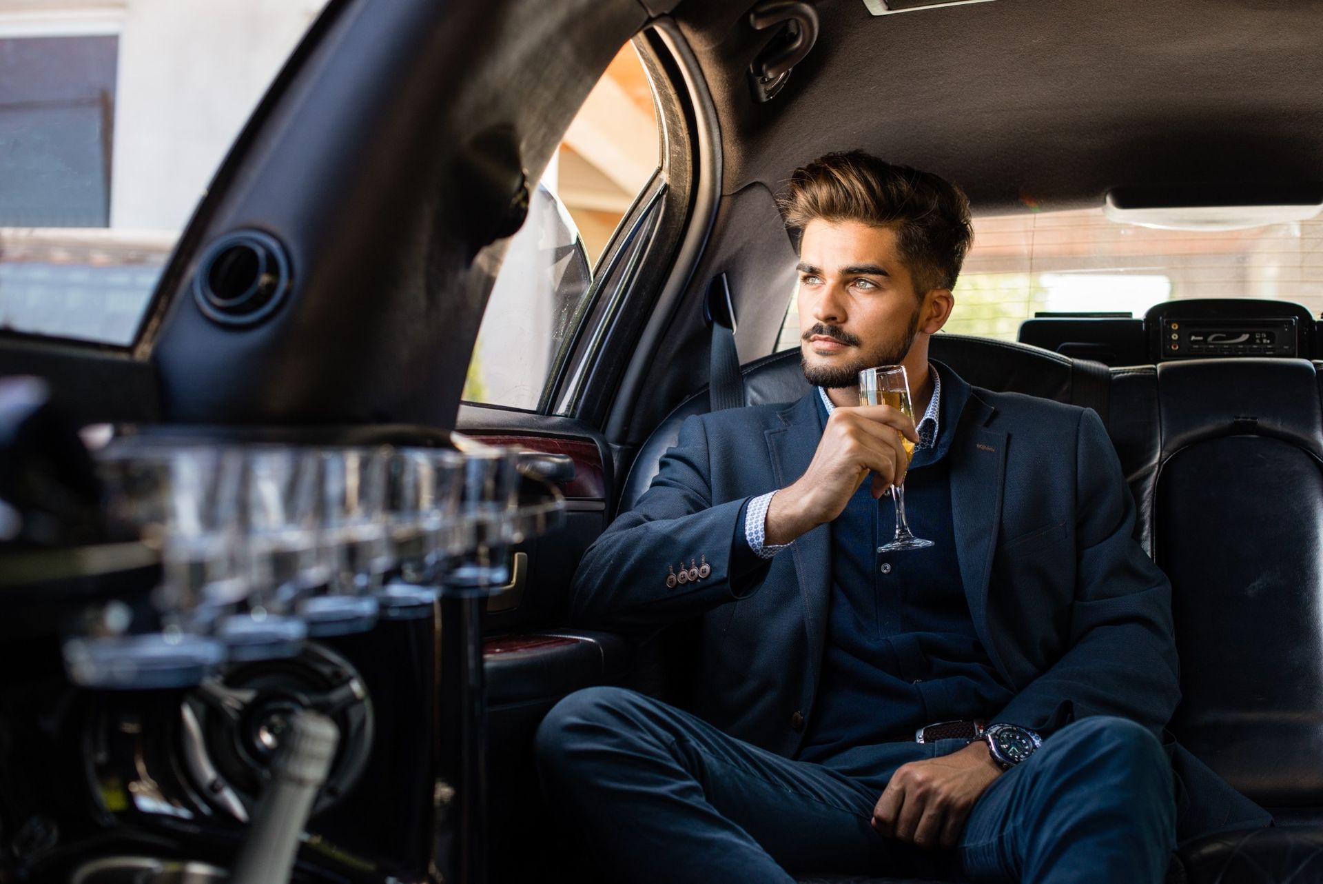 A man is sitting in the back seat of a limousine drinking a glass of champagne.