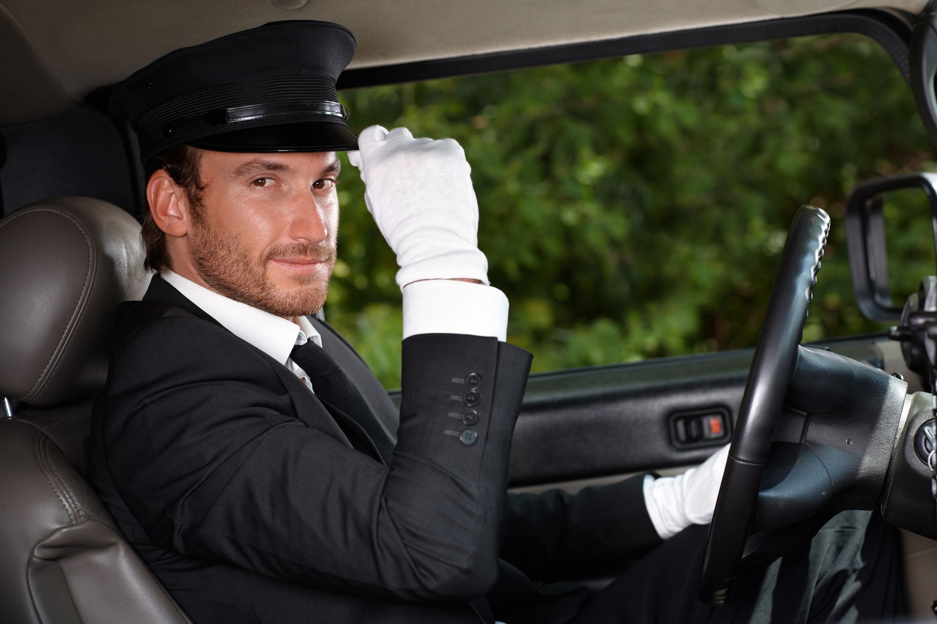 A man in a suit and white gloves is driving a car.