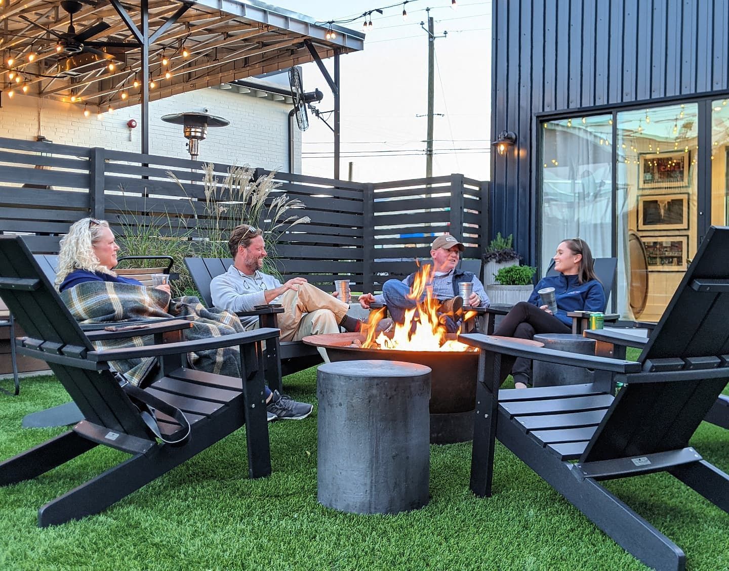 Four people gathered around a fire pit in an outdoor lounge area, enjoying drinks and conversation.