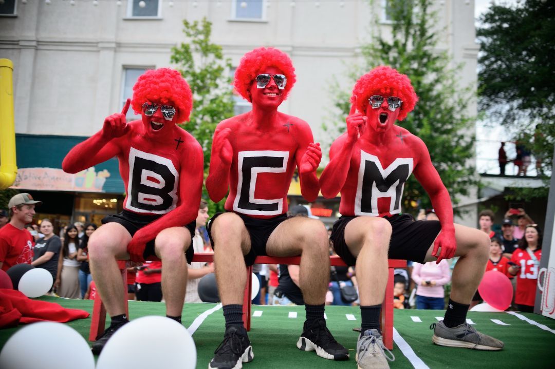 Three people with red body paint and wigs spell