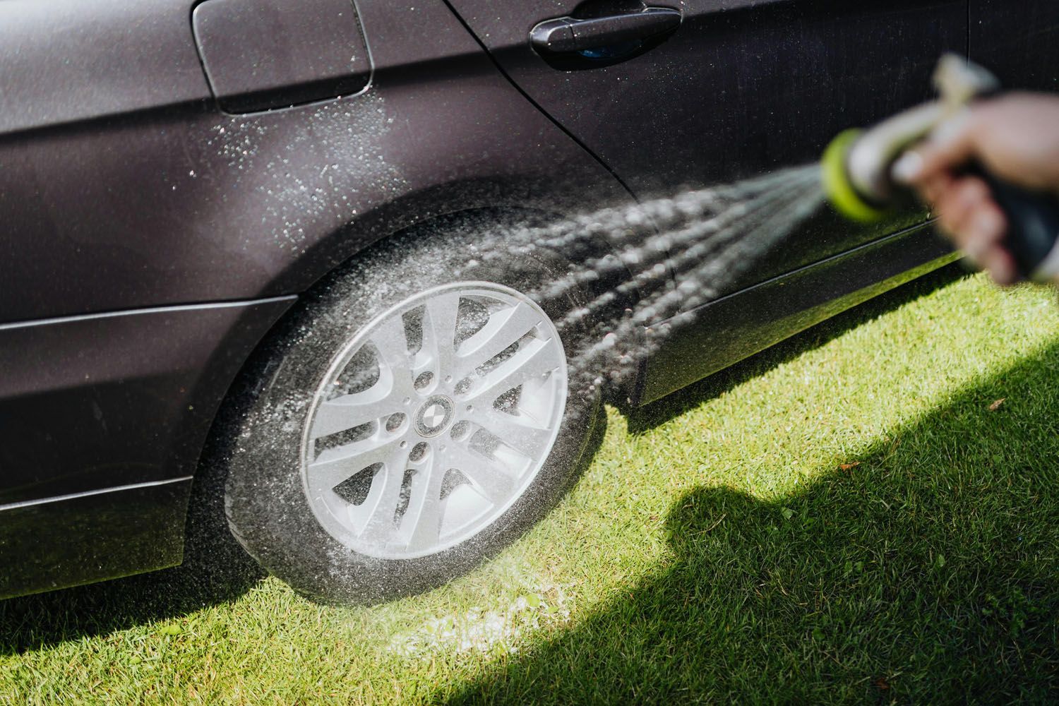 A person is spraying water on a car wheel with a hose.