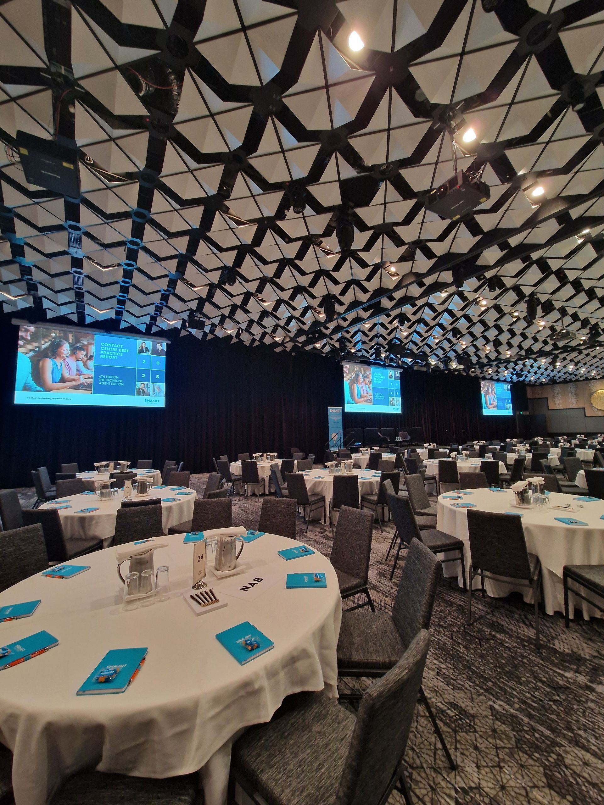 Conference room setup with round tables, chairs, screens, and patterned ceiling.