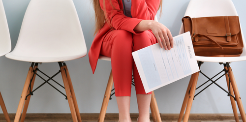 Woman in red suit holds documents, sitting in chair, waiting for an interview. Leather bag on the chair.
