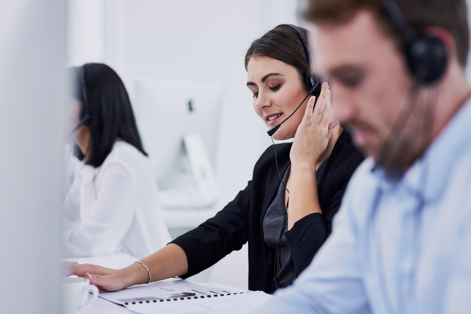A woman wearing a headset is talking on a phone in a call center.