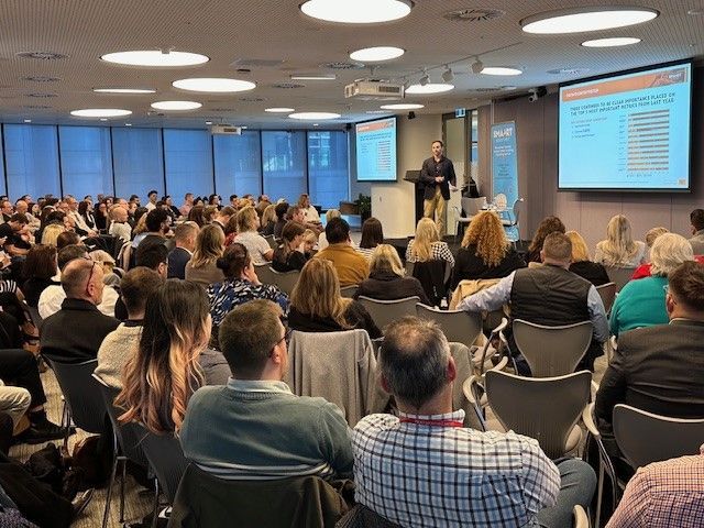 A large group of people are sitting in a conference room watching a presentation.