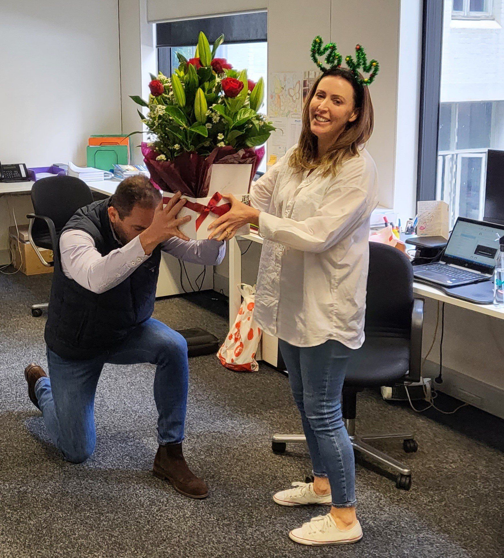 A man is kneeling down in front of a woman holding a bouquet of flowers.