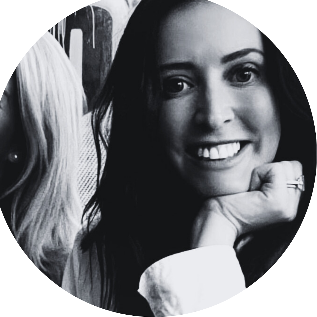 A black and white photo of a woman smiling with her hand on her chin