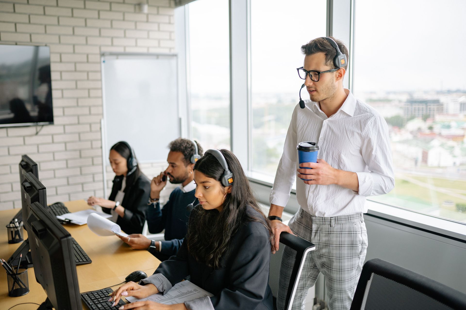 Office team working at desks while a man stands holding a coffee cup in a bright workspace.