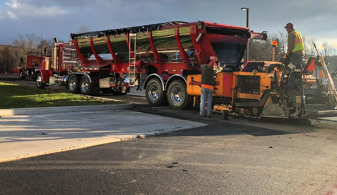 Trout River Industries Live Bottom unloading asphalt into a paver while a crew pave a road