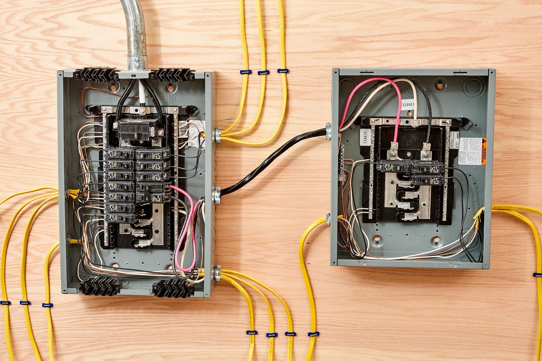 Two electrical panels are connected to each other on a wooden wall.