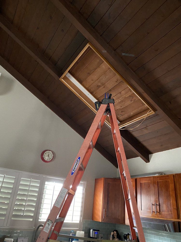 A ladder is sitting under a wooden ceiling in a kitchen.