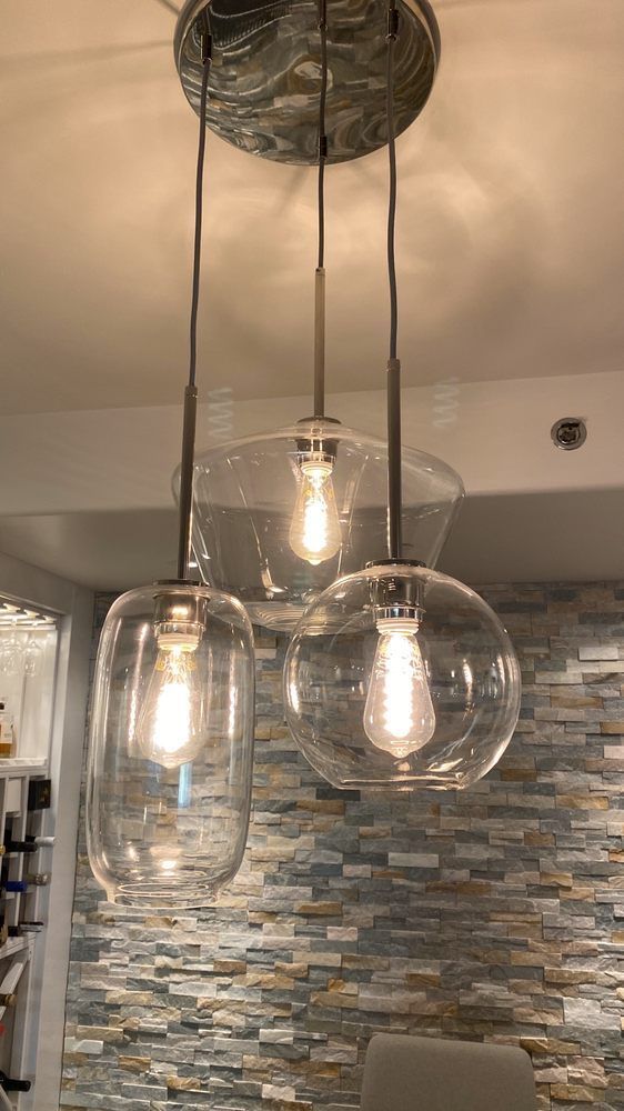 A pendant light with three clear glass shades is hanging from the ceiling in a kitchen.