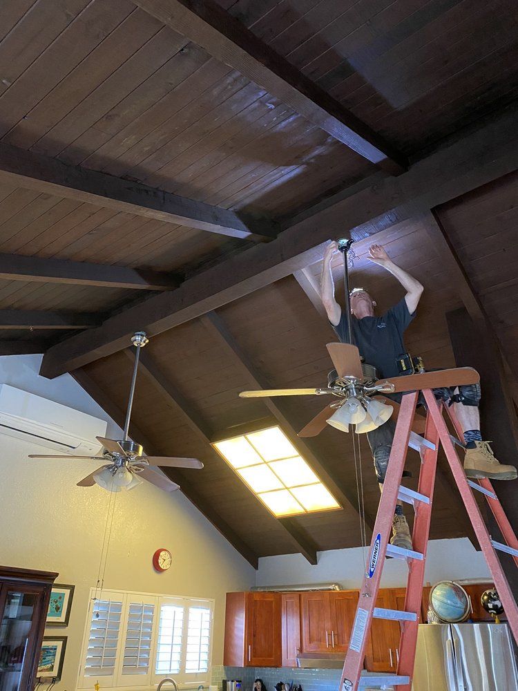 A man is standing on a ladder fixing a ceiling fan.