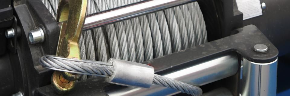 Close-up of a winch with steel cable wrapped around the spool. The cable is secured by a metal clip.