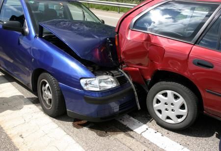 Blue car and red car involved in a head-to-rear-end collision on a road, both damaged.