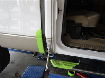 Truck door being repaired, taped with green tape, on a blue lift.