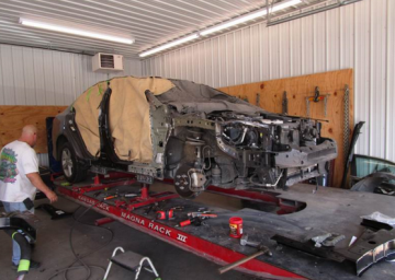 Car on a frame rack in a repair shop; a person works on the vehicle.