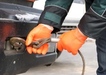 Person in orange gloves connecting a tow cable to the hitch of a black car.