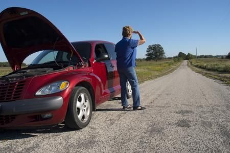 Red car with open hood, stranded on a rural road. A person stands beside it, holding a hand to their forehead.