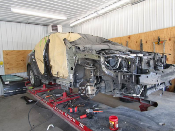 Car being repaired in a body shop, partially disassembled on a lift; tan covering on the left.
