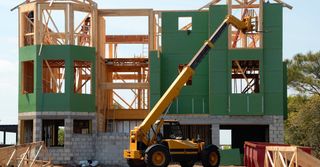 A large house is being built with a yellow crane in front of it.