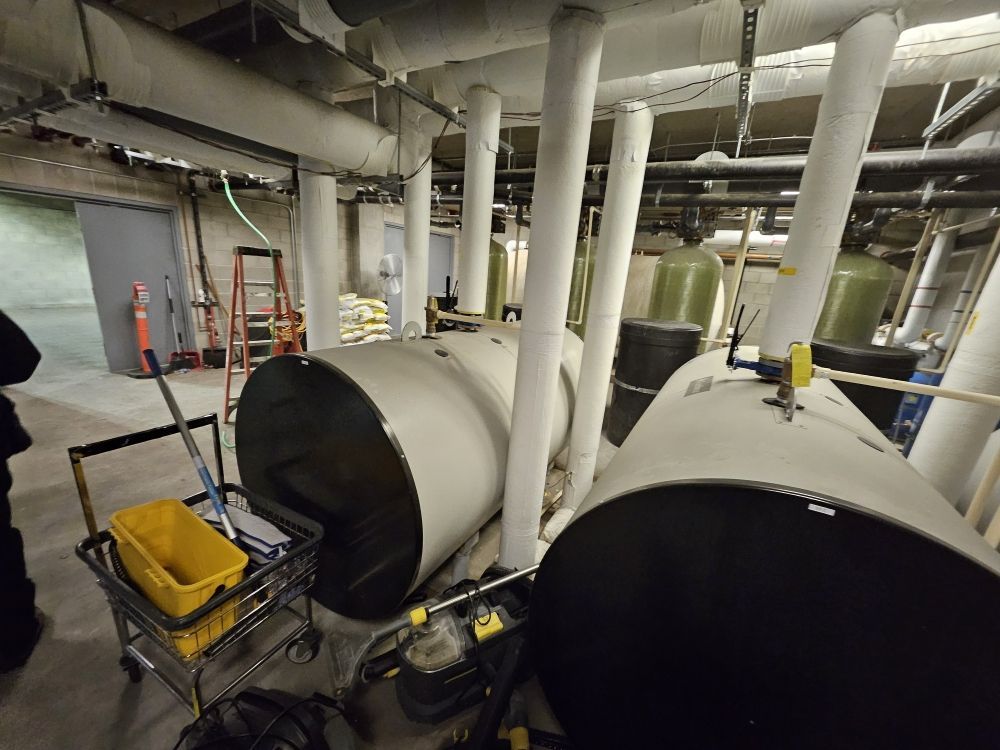 Basement with large cylindrical tanks, pipes, and construction equipment. Gray, white, black, and yellow colors.