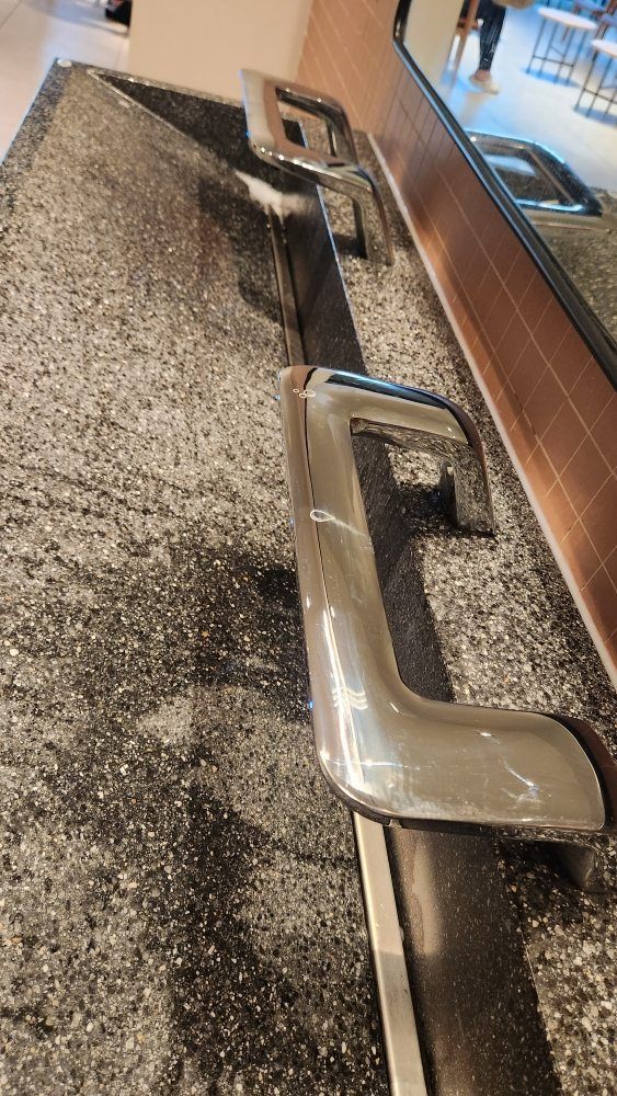 Stainless steel handrails along a speckled gray wall, near a wood-paneled wall and mirror.