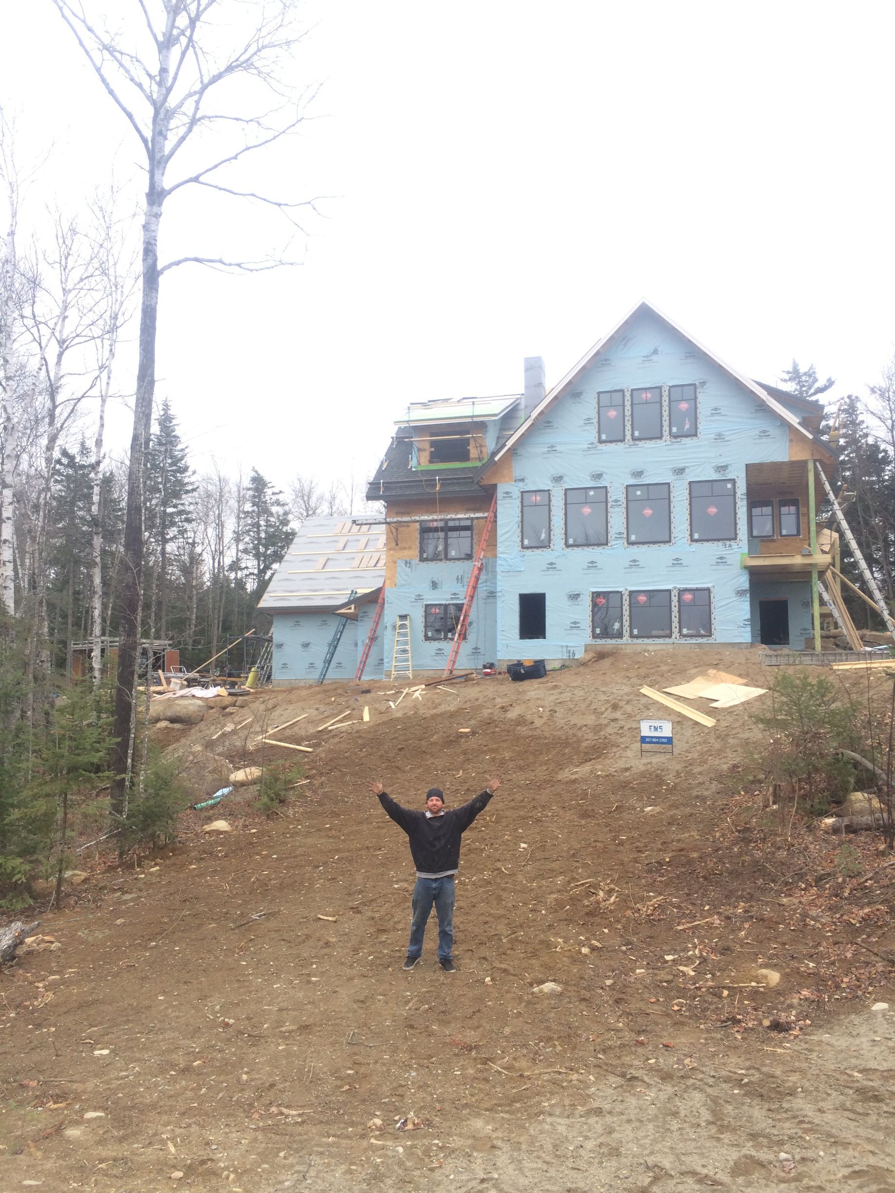 Dark gray tiled roof on a white house, chimney, skylight, and gutter visible against a cloudy sky.