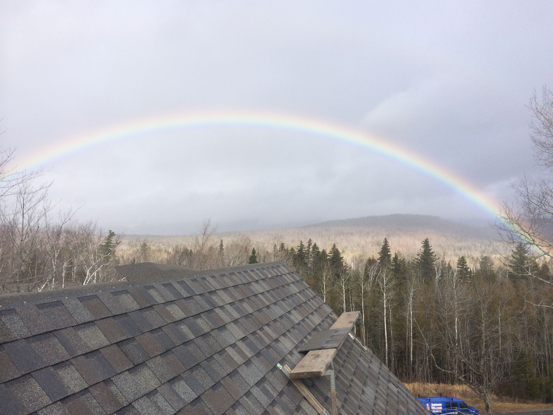 Roofer in blue hard hat works on a wooden roof structure, attaching a tool. Sunny day.
