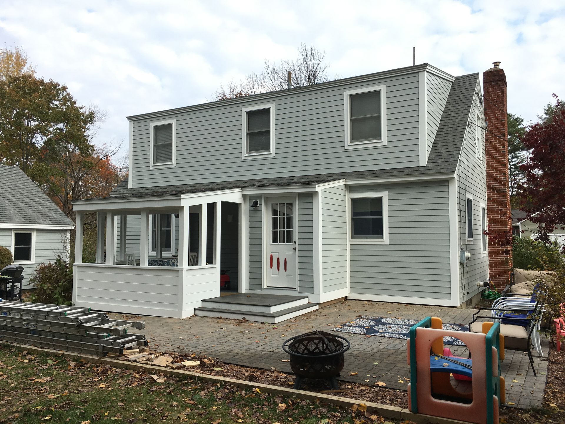 Roofer in safety gear repairs shingles on a roof under a blue sky, near the edge of a house.