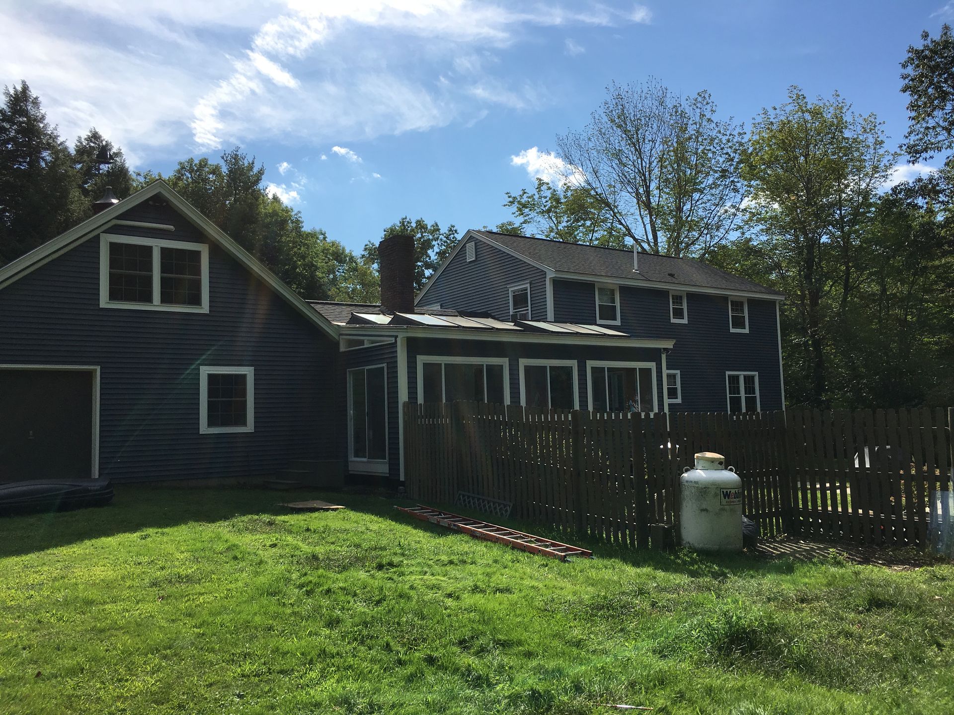Gray metal roof with a chimney and skylight on a white house against a blue sky.