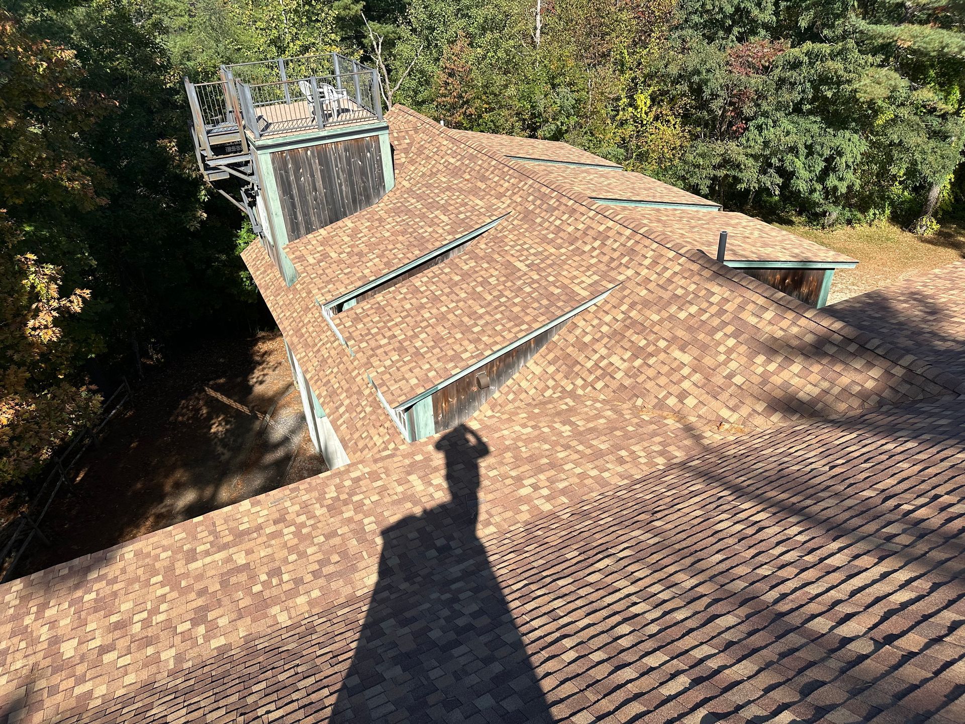 Roofer kneeling, using a nail gun to install asphalt shingles on a roof.
