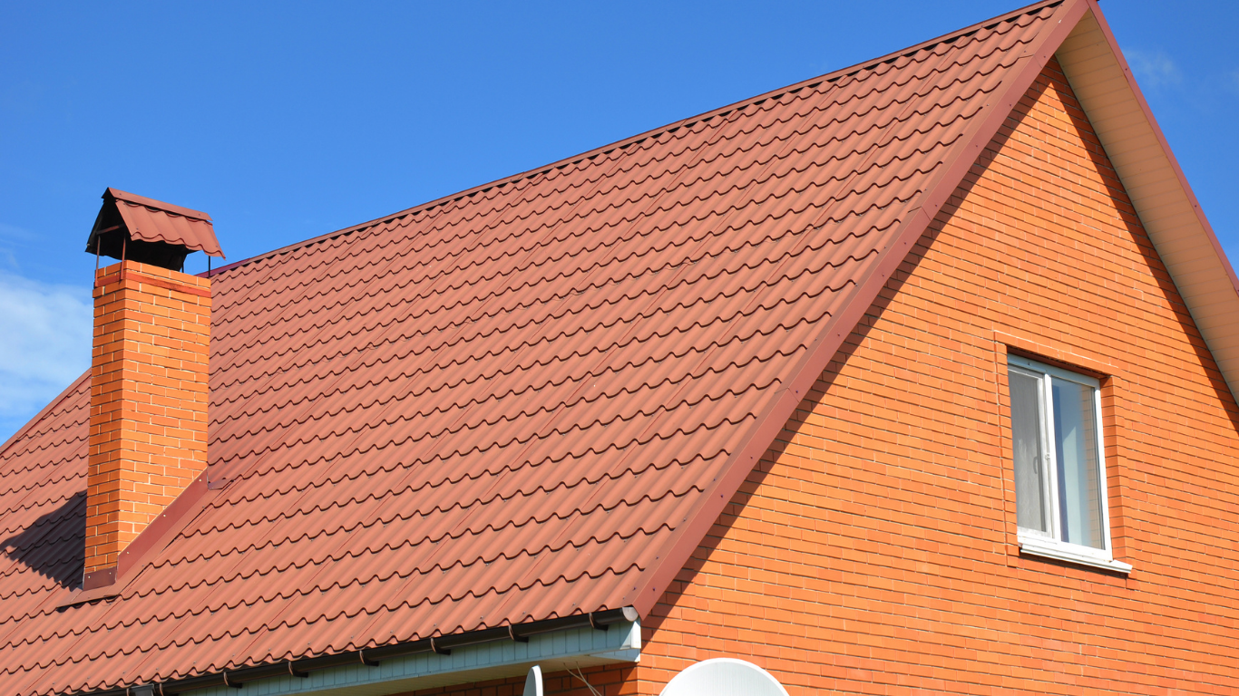 Brick house with a red roof, chimney, and window against a blue sky.