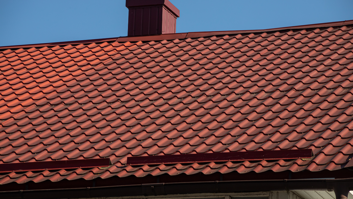 Red tile roof with chimney against a blue sky.