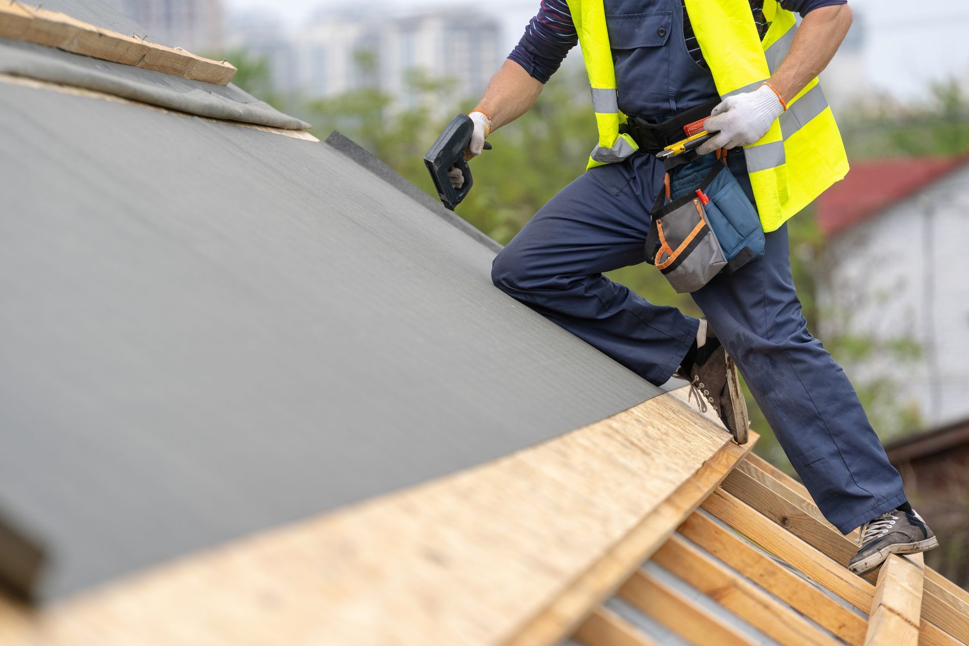 Roofer in safety vest, installing roofing material on a house roof.