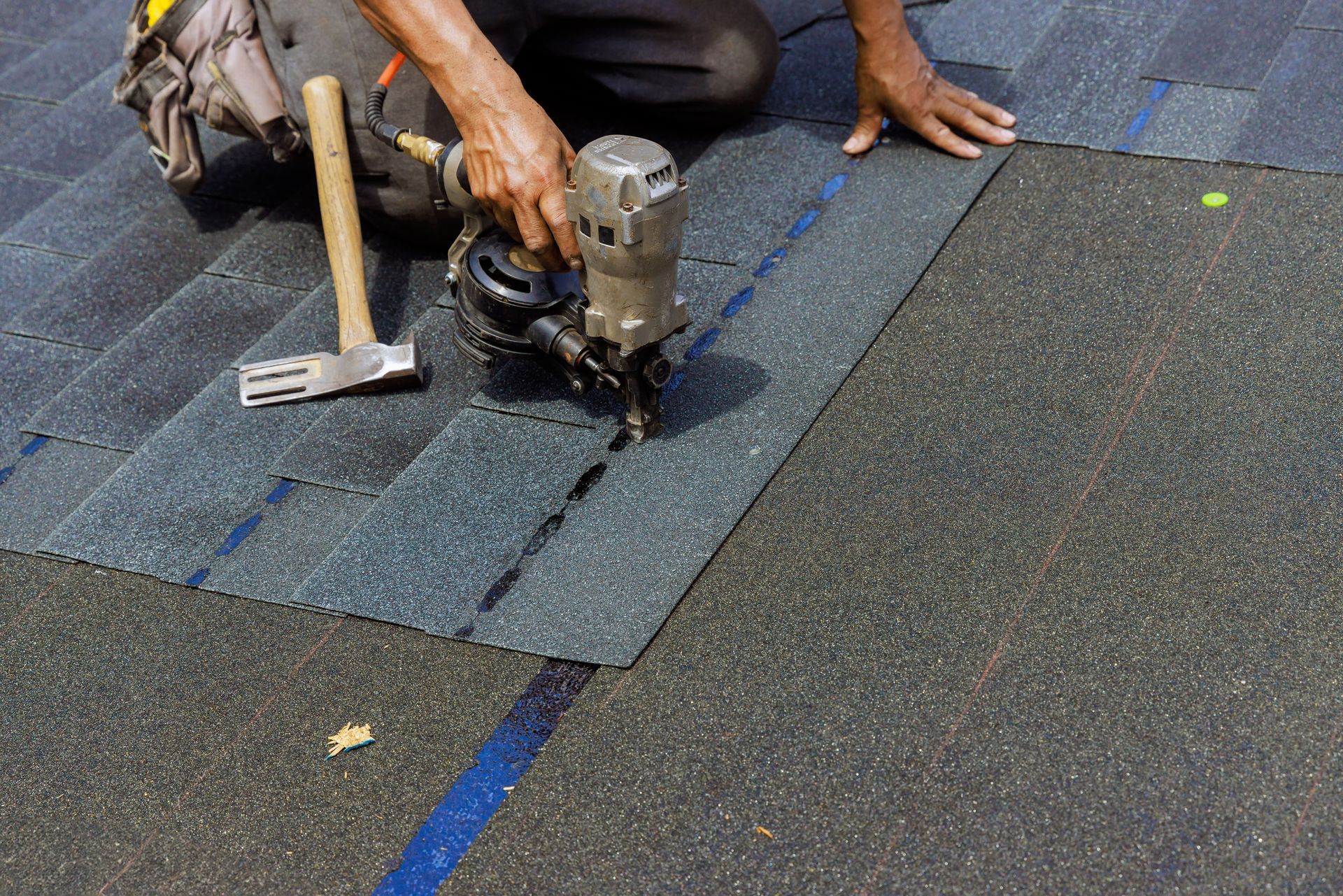 Person using a nail gun to install asphalt shingles on a roof.