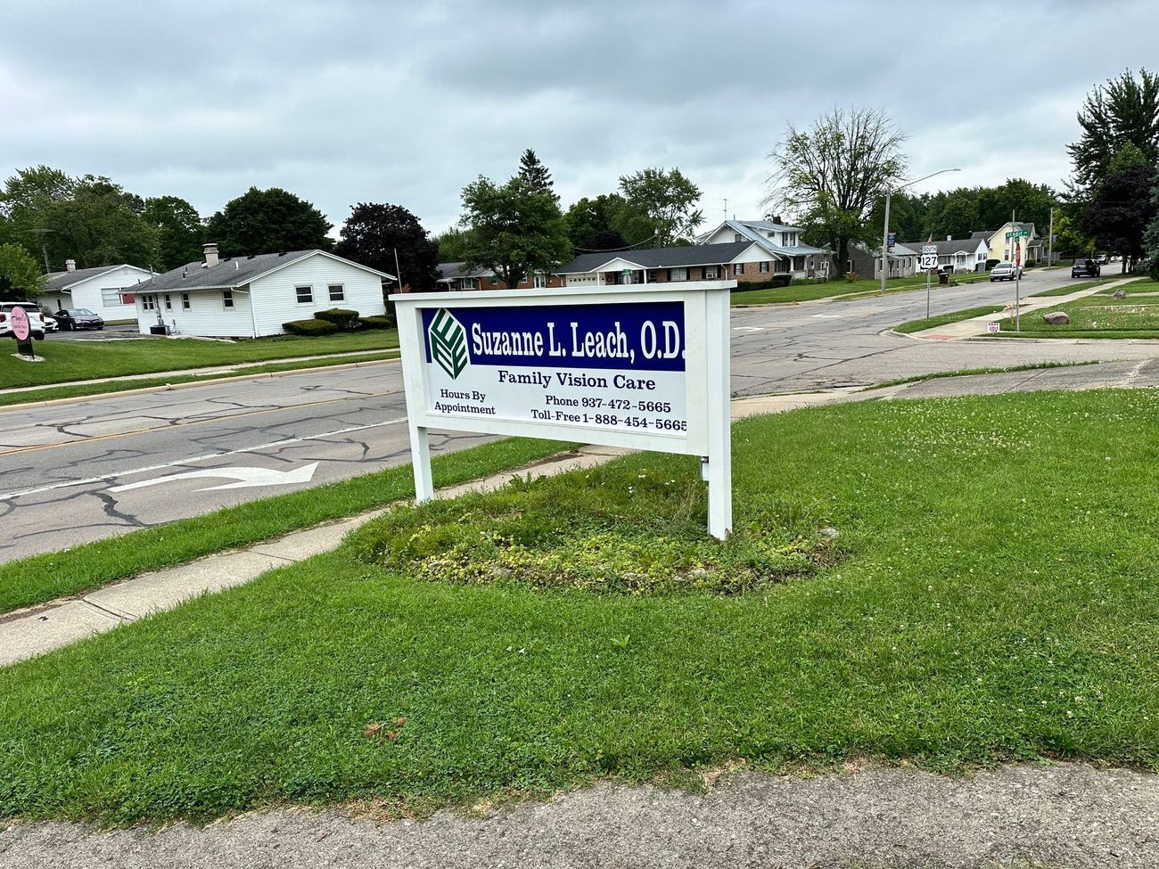 A sign for a dentist is sitting in the grass on the side of the road.