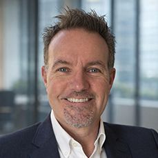 A bald man wearing glasses and a blue shirt smiles for the camera