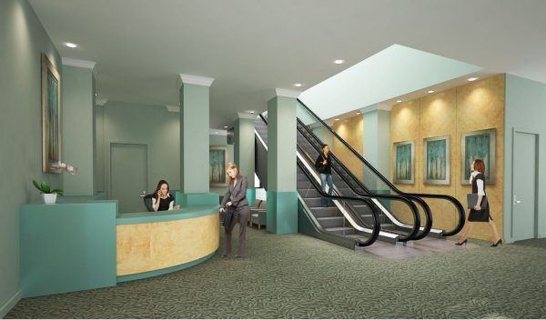 Modern lobby interior with a curved reception desk, an escalator, framed artwork, and people walking through the space.