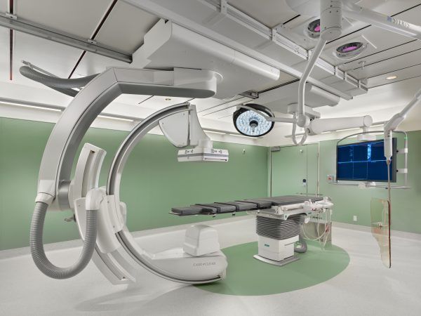 A medical examination room featuring a robotic C-arm imaging system positioned over a procedure table.