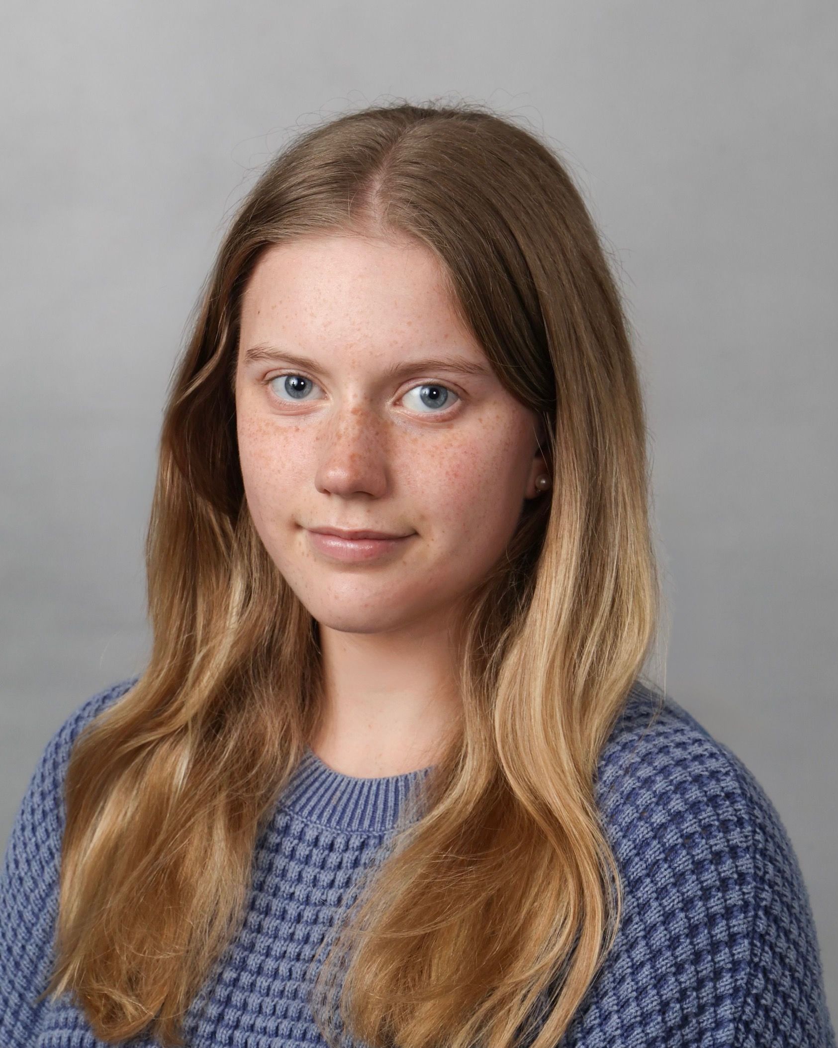 A young woman with long blonde hair and blue eyes is wearing a blue sweater.