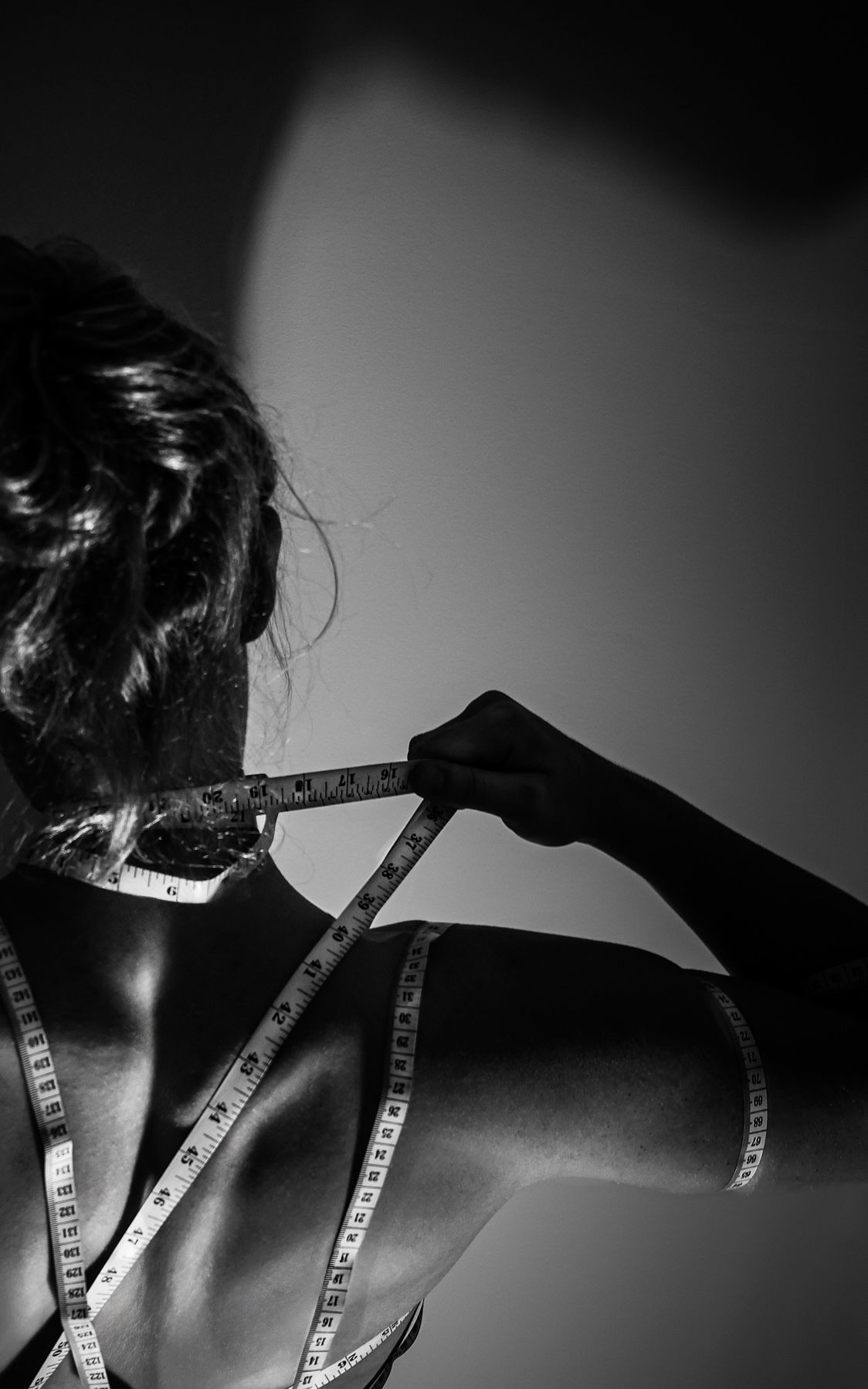 A woman is measuring her shoulder with a tape measure.