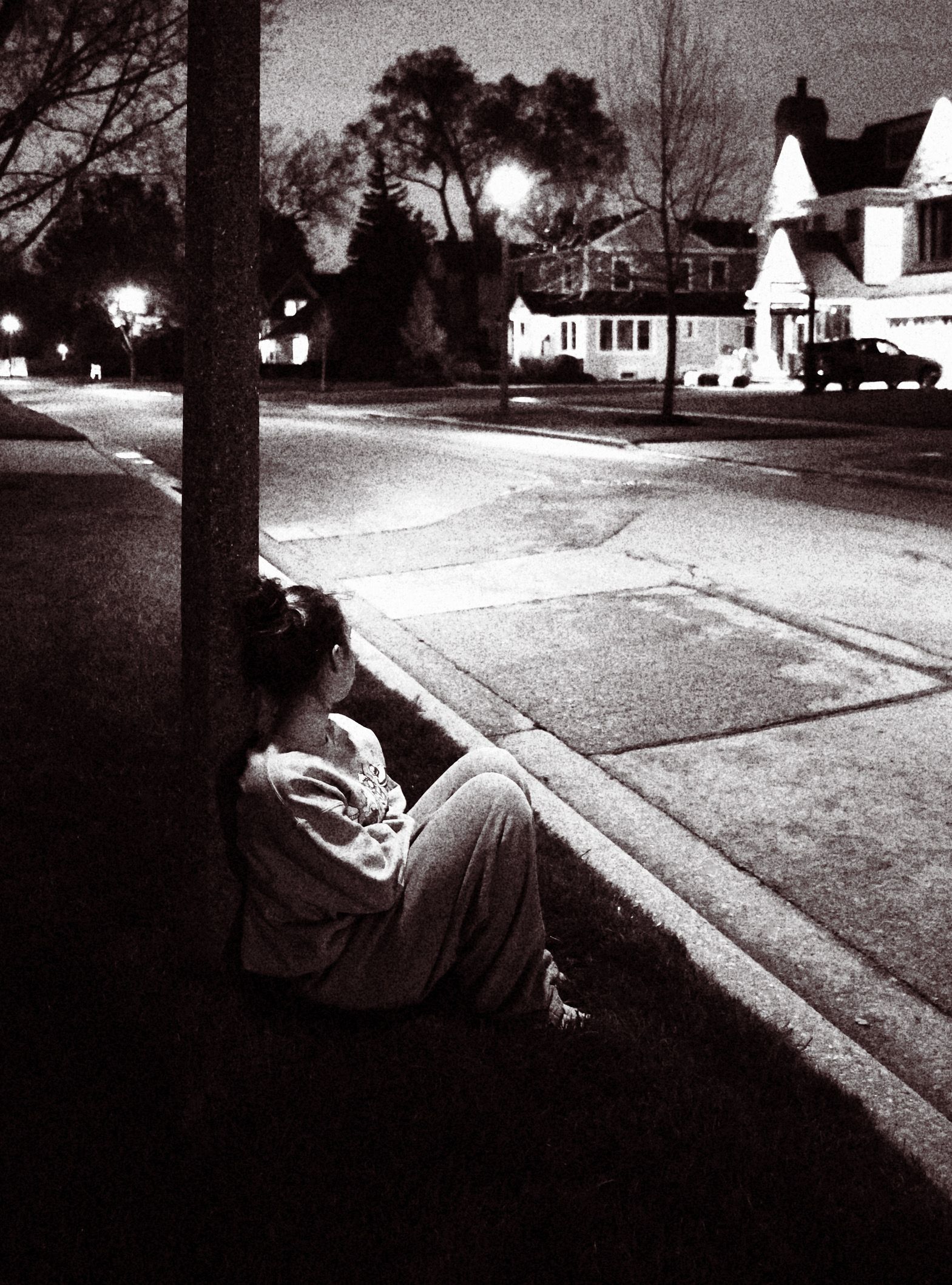 A black and white photo of a person leaning against a pole
