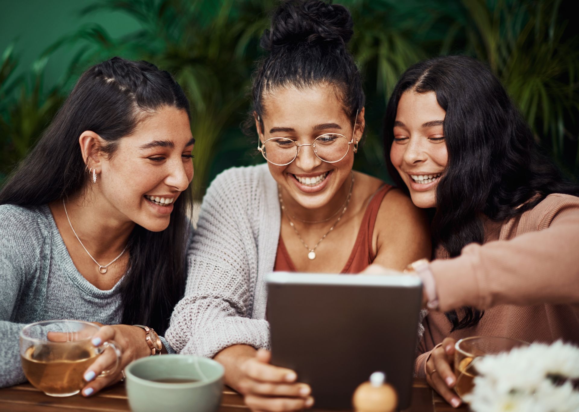 Three women are sitting at a table looking at a tablet.