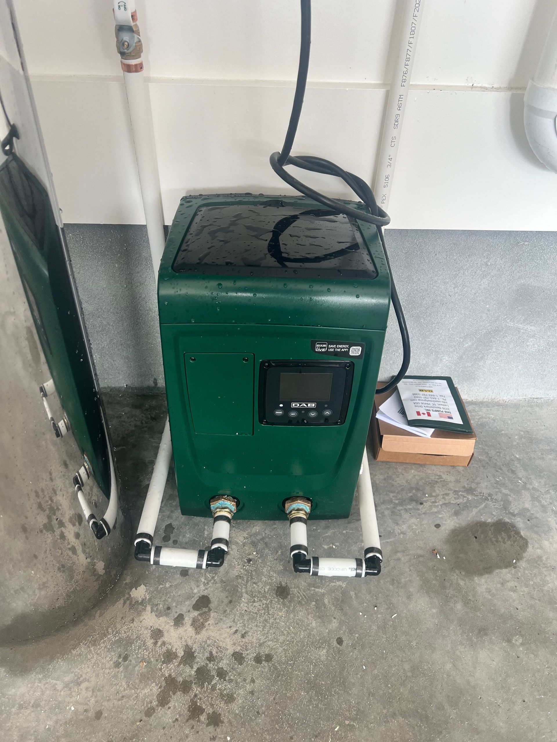 Green spa heater with digital display, pipes, and power cord in a utility area.