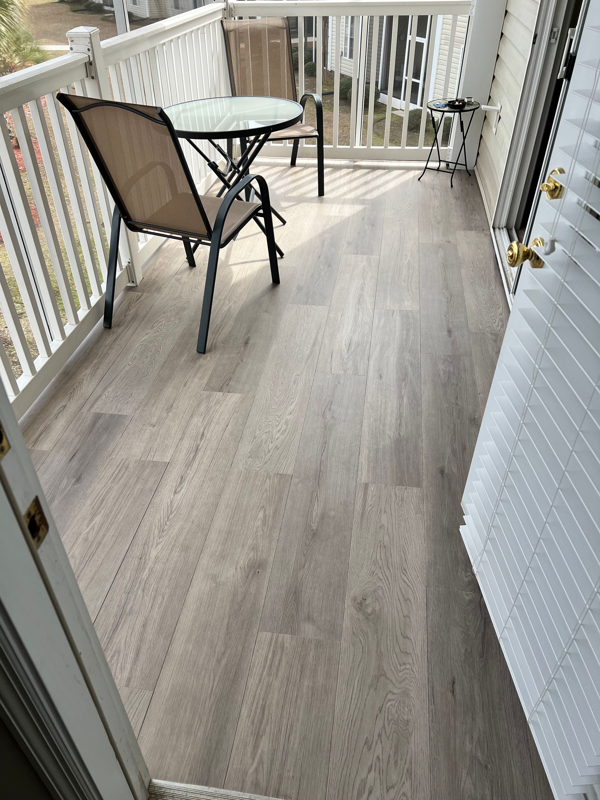 Small deck with light gray flooring, small round table, two chairs, white railing.