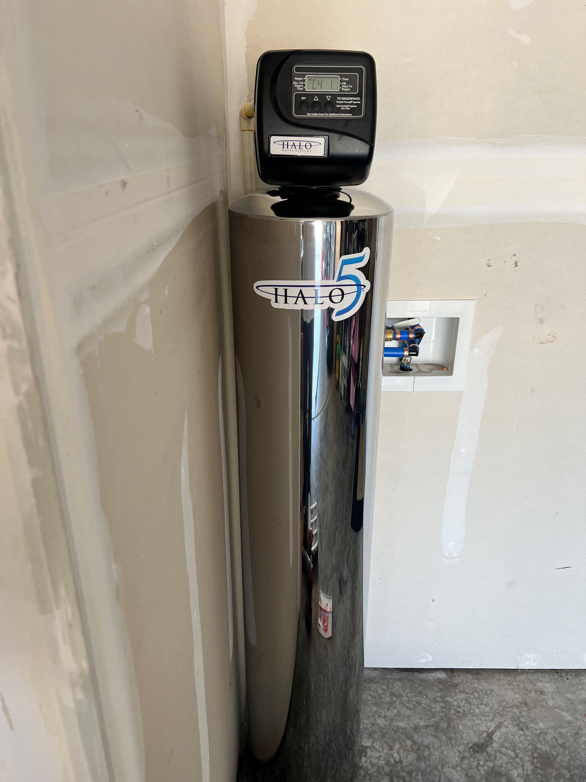 Chrome water softener tank with digital display in a utility room.