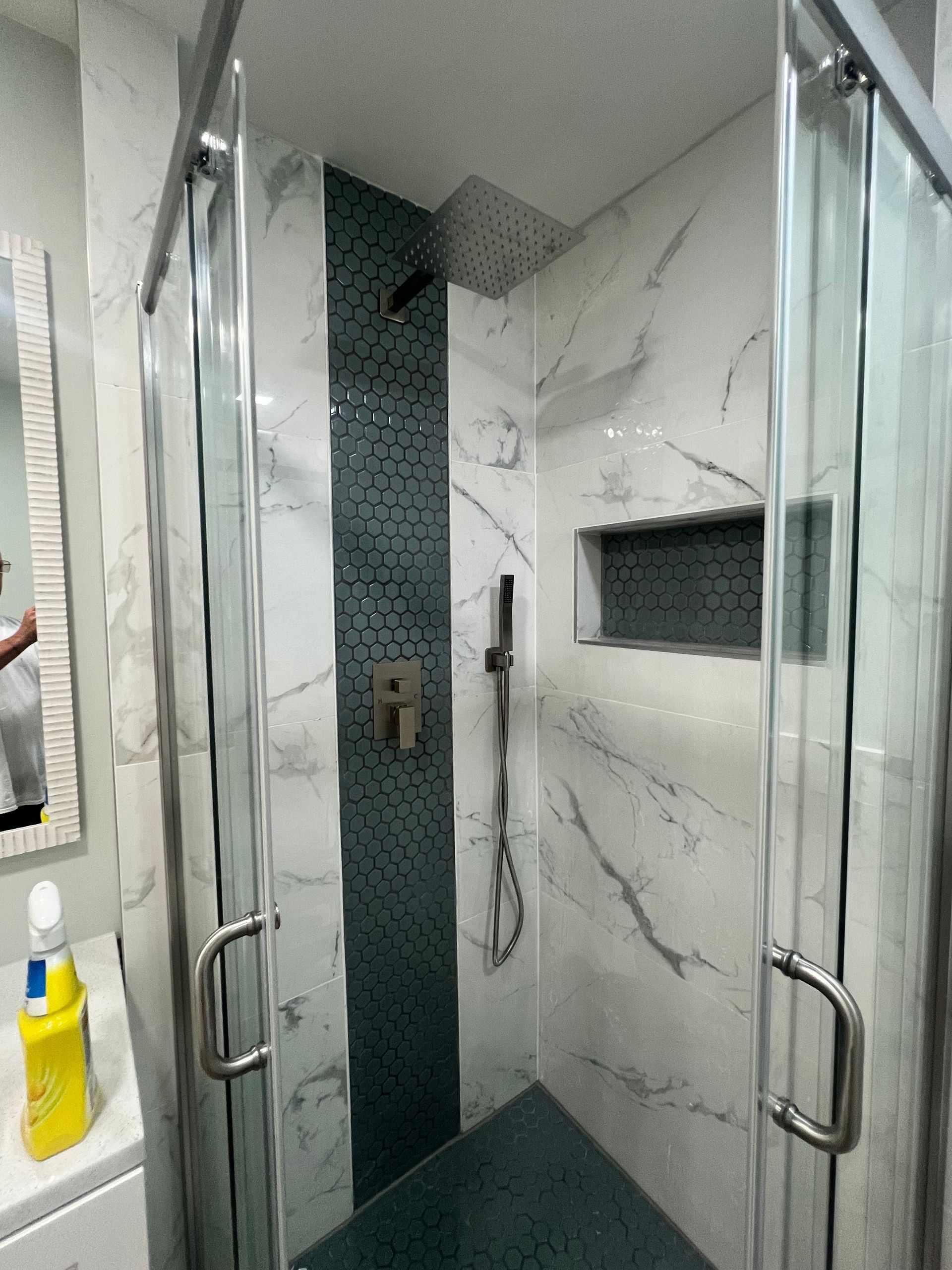A modern shower with glass doors. White marble-look tile, a teal accent strip, and a built-in shelf.